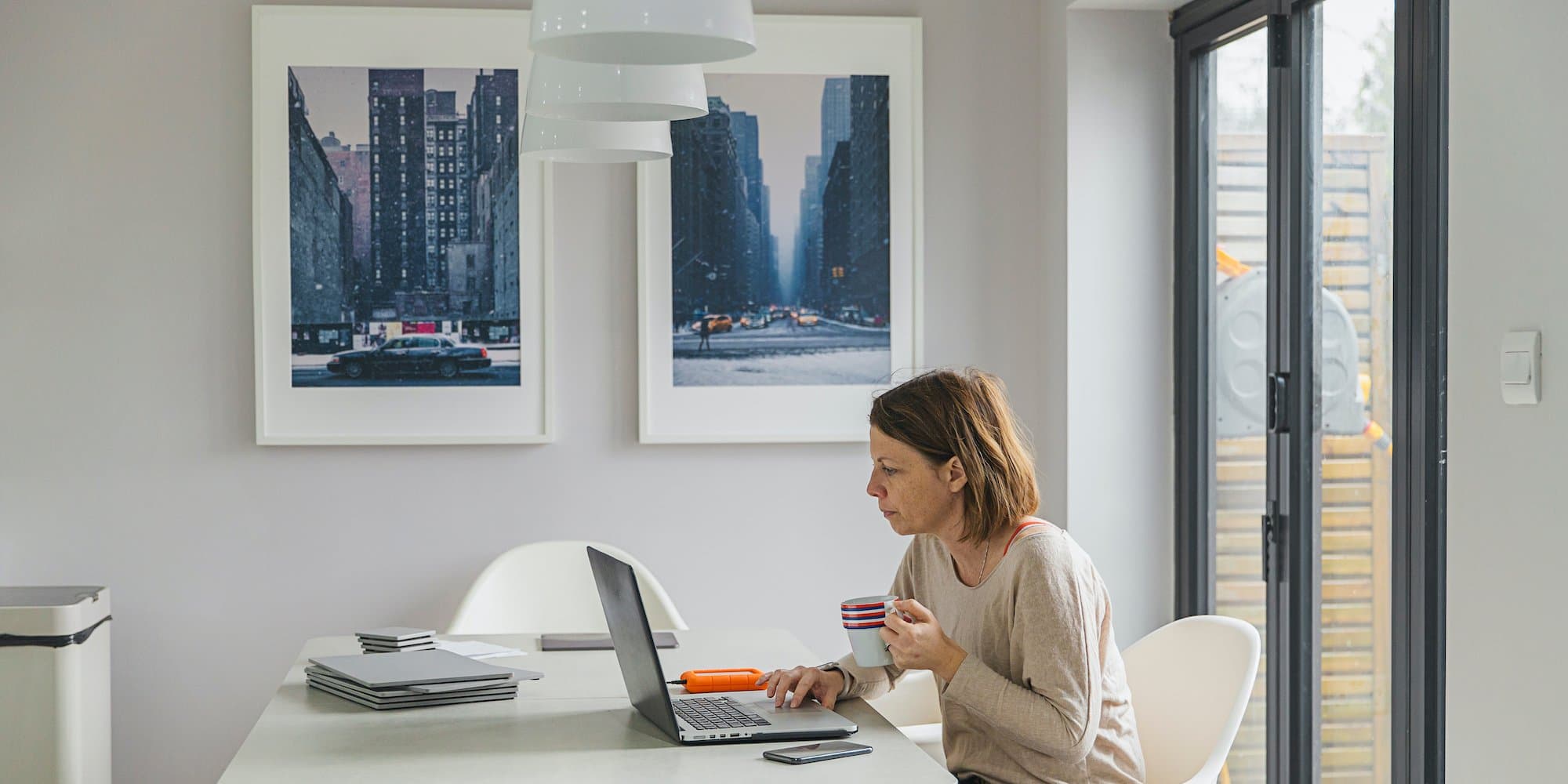 person sitting at table in home working on laptop while drinking coffee