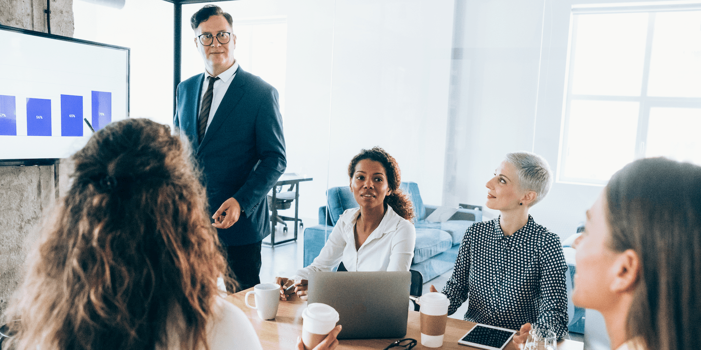 group of colleagues sitting in a meeting listening someone standing and presenting