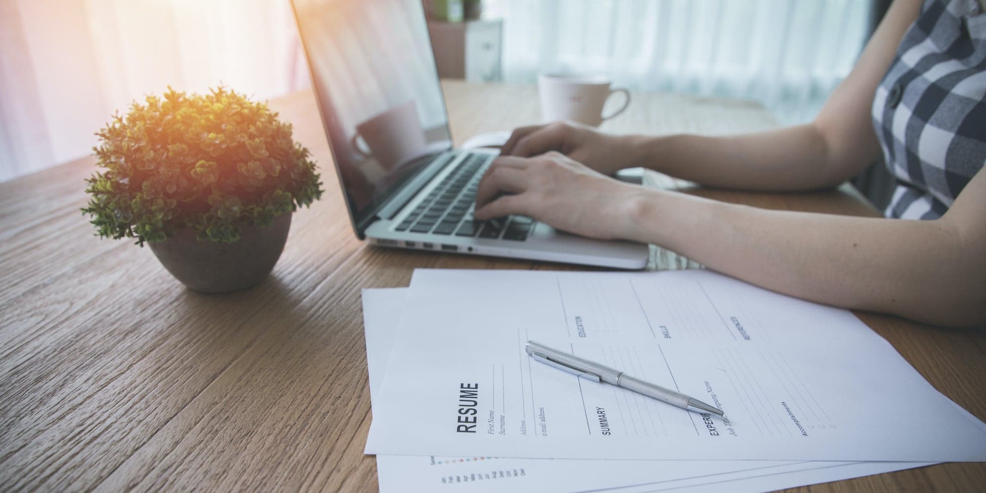 Hands on laptop keyboard next to resume outline paper