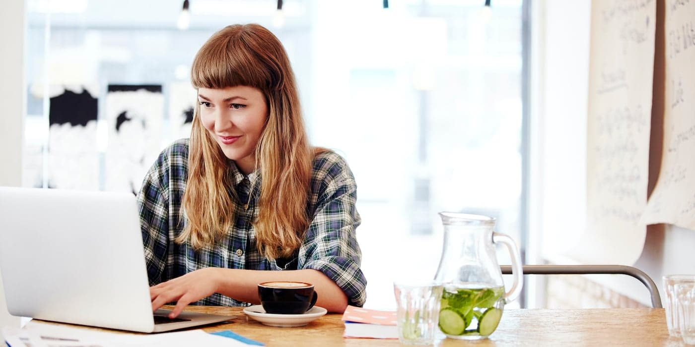 person with long hair working on a laptop in a coffeeshop