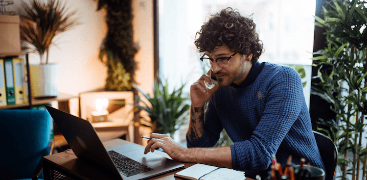 person working on a laptop and talking on the phone at a desk at home