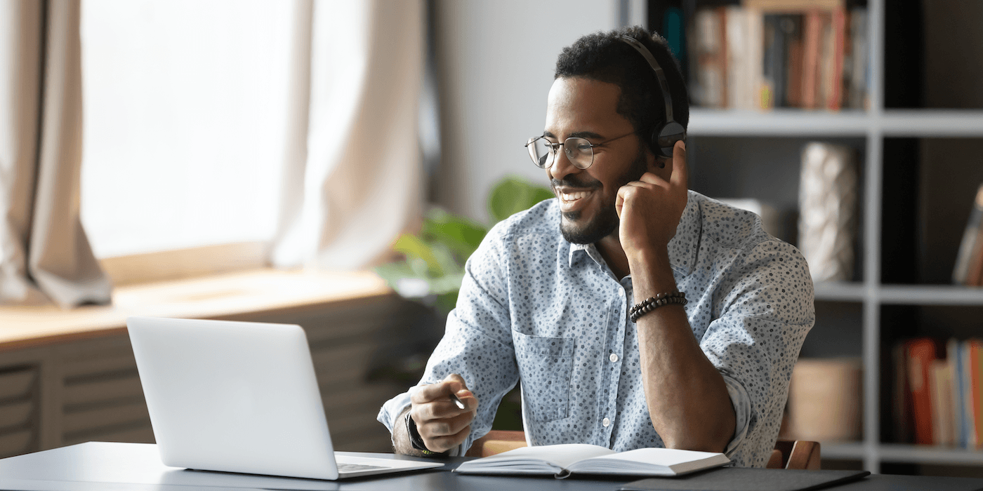 person sitting at a table at home in front of their laptop wearing headphones