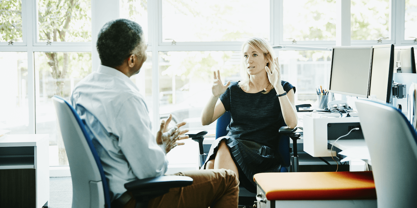 two people sitting in an office and speaking to each other