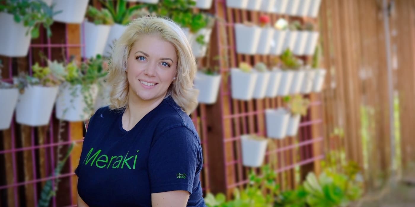 person with short blonde hair standing next to a wall of plants