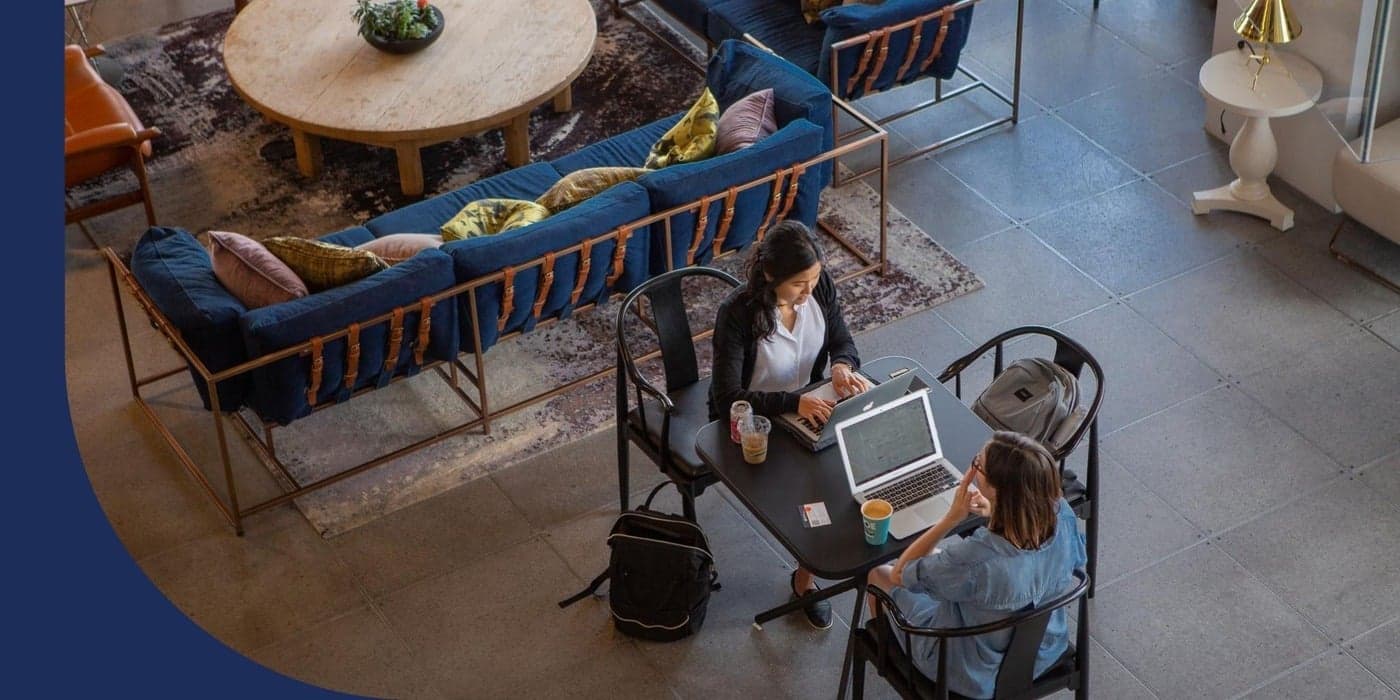 Two people sitting at a table while working on their laptops in an open-plan office.