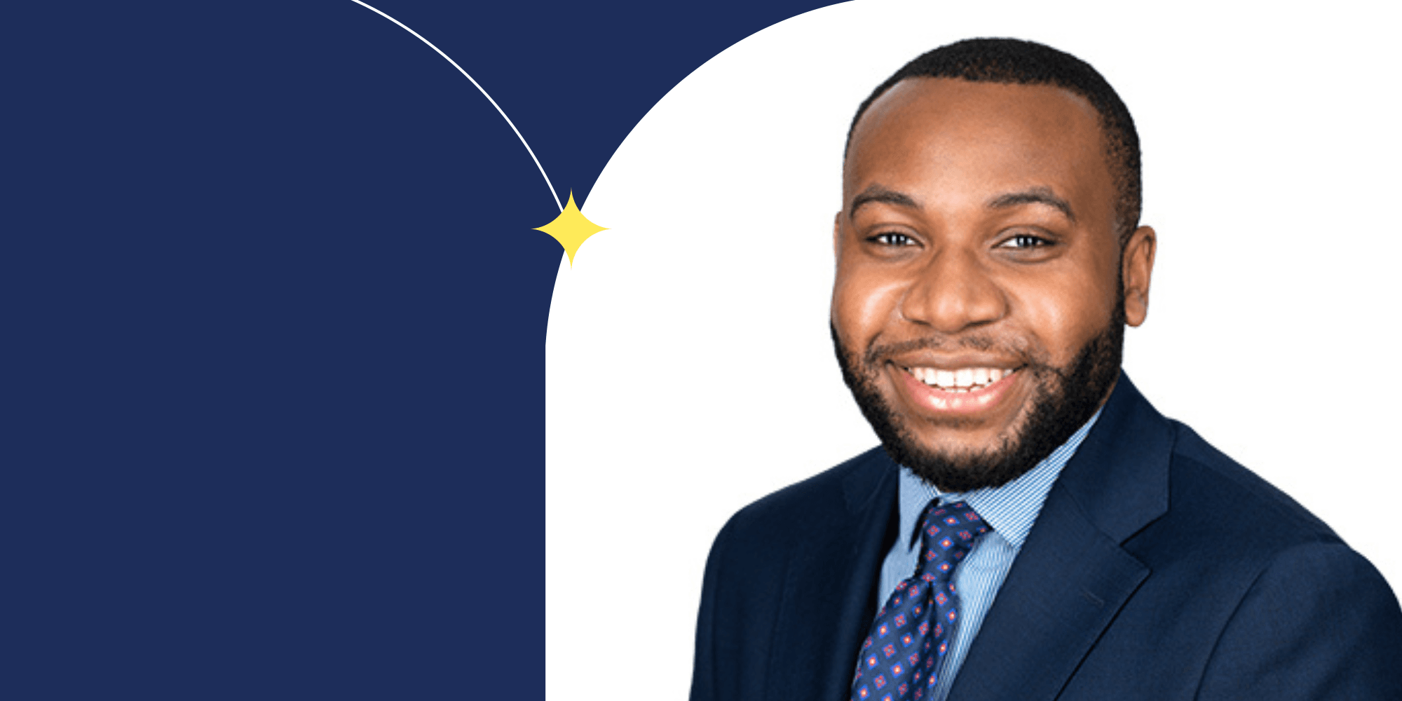 A smiling person facing the camera. They are wearing a blue suit jacker, a blue collared shirt, and a blue tie. The person has a beard.