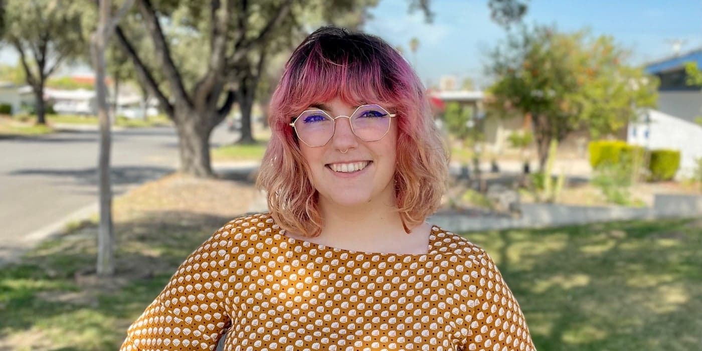 person with pink hair and glasses smiling