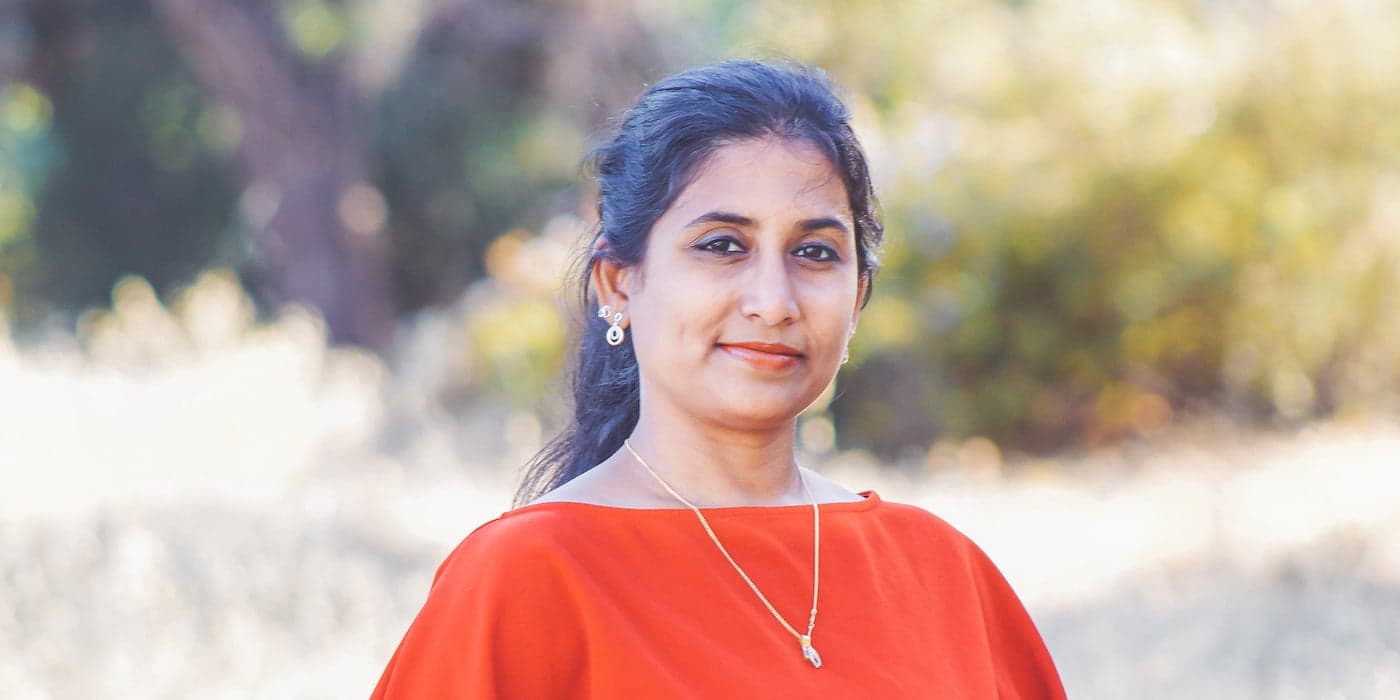 person with dark hair pulled back wearing an orange blouse