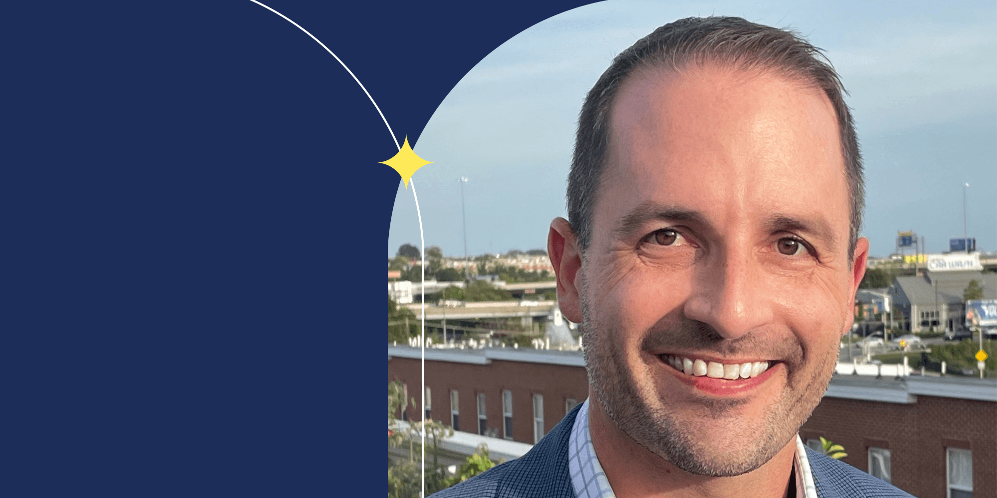 A smiling person facing the camera. They have short hair and are wearing a collared shirt with a blue jacket.