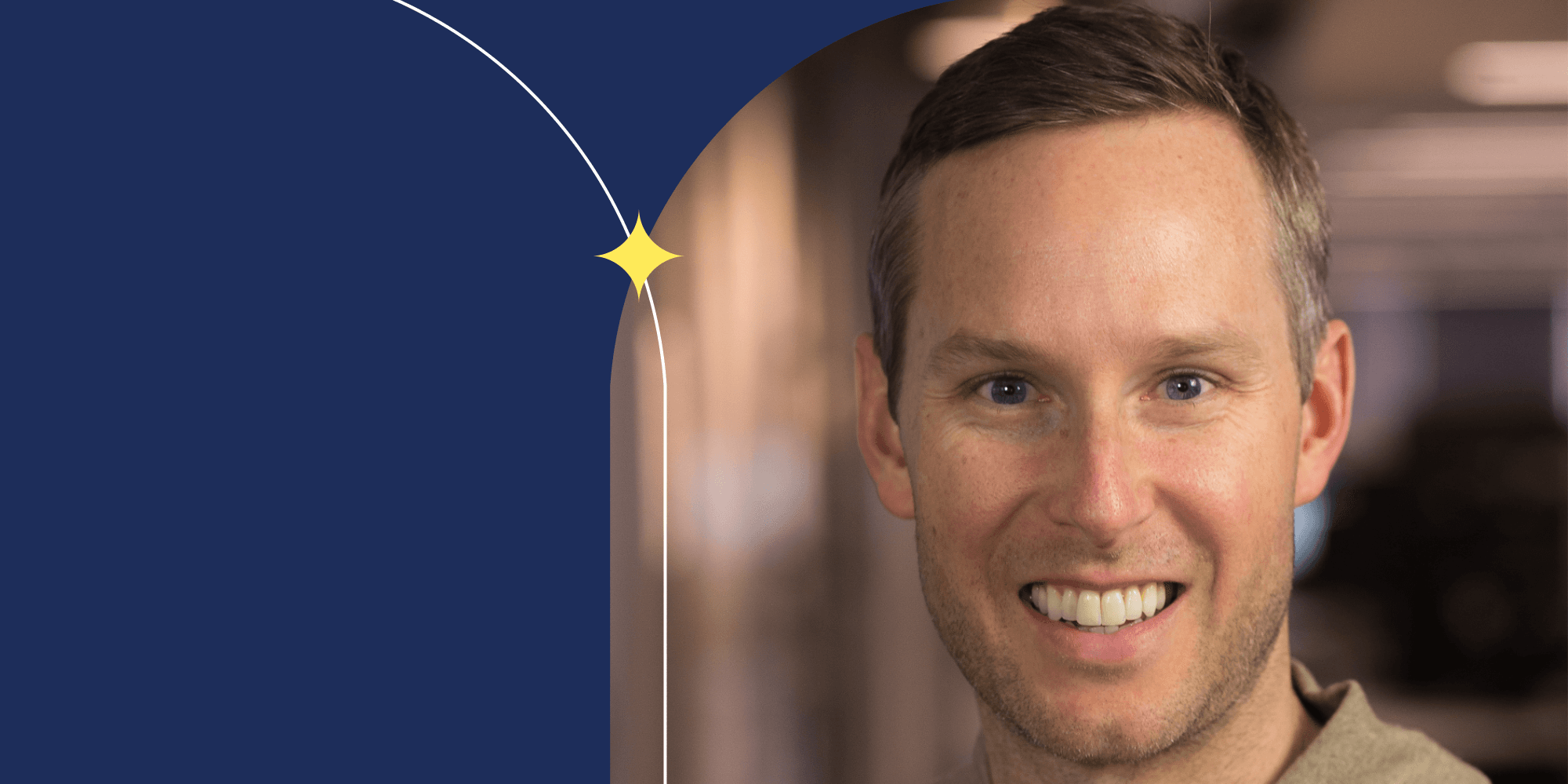 A smiling person facing the camera. They have short hair and blue eyes.