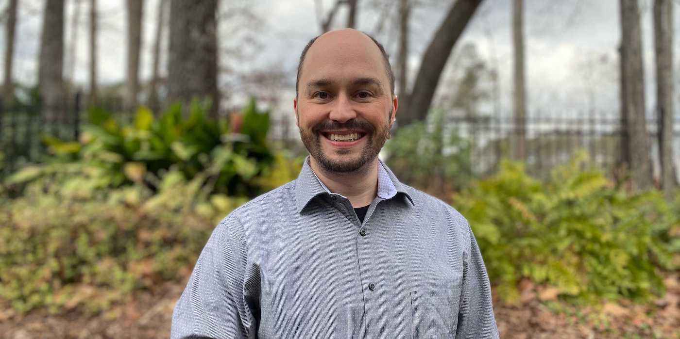 smiling person standing in front of green bushes