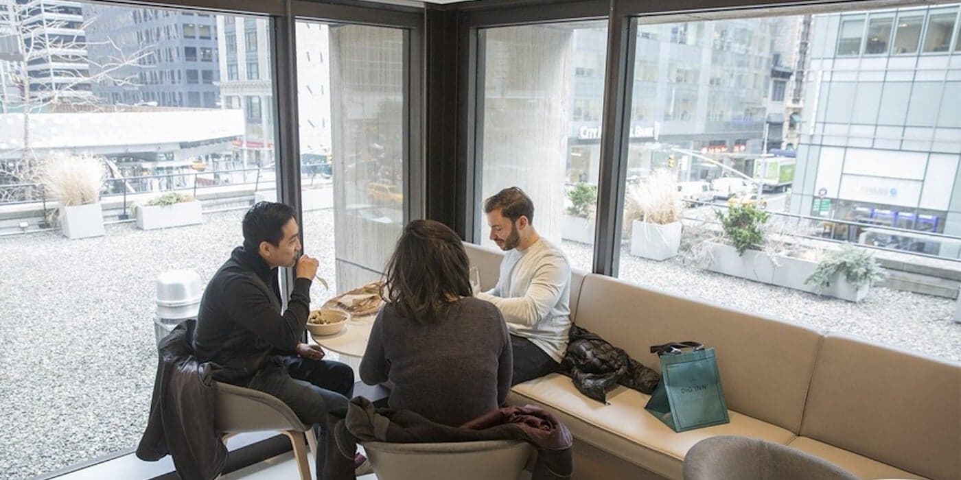 people having lunch together by a large window in an office