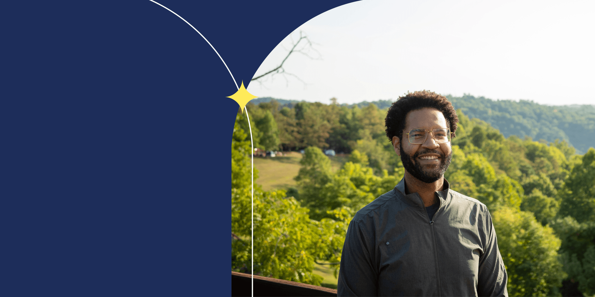 A person facing the camera and wearing a green shirt. The person is wearing glasses. Lush trees can be seen behind them.