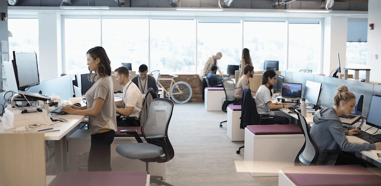 people working in an office, one using a standing desk,
