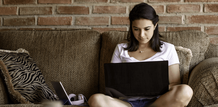 young person sitting on the couch cross-legged working on a laptop